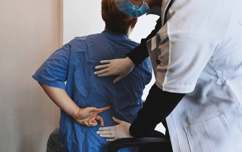 lekarz podczas oględzin pleców pacjenta, grafika przekierowująca do podstrony poradni leczenia bólu